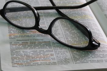 Raamatun sivu, jonka päällä mustasankaiset silmälasit
