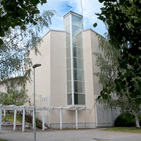 Vaalea kirkkorakennus edestä kuvattuna, vieressä vihreitä havupuita.