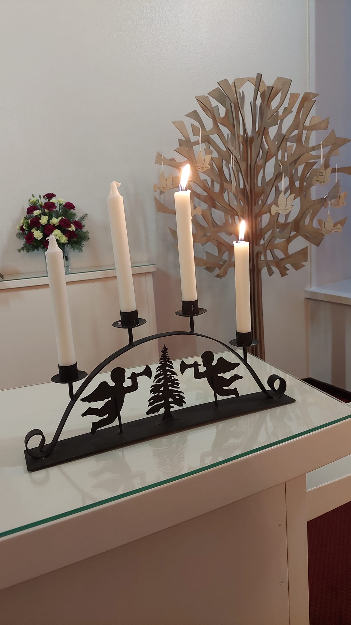 Riistaveden kirkon alttaripöydällä palaa kaksi kynttilää. Taustalla kastepuu.