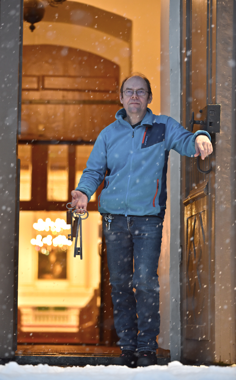 Vahtimestari avainnipun kanssa kirkon pääovella lumisateessa.