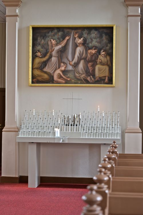 Tuomiokirkon lähetyskynttelikössä palaa muutama kynttilä, yläpuolella maalaus, jossa ihmisiä ja vesiputous.