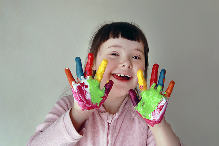 Iloinen tyttö, jonka kädet on maalattu eri värisllä maaleilla.