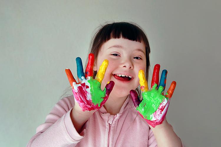 Tyttö näyttää käsiä, joissa paljon eri värisiä maaleja.