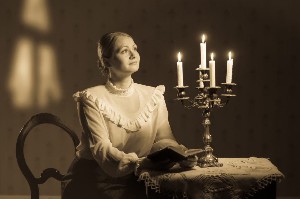 Musiikkidraama Amalia 1800-luvun asussa oleva nainen lukee kirjaa kynttilänvalossa