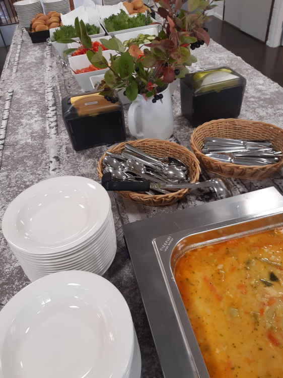 Lautasia pöydälla, keittokanttilassa keittoa, leikkeleitä ja ruokailuvälineitä