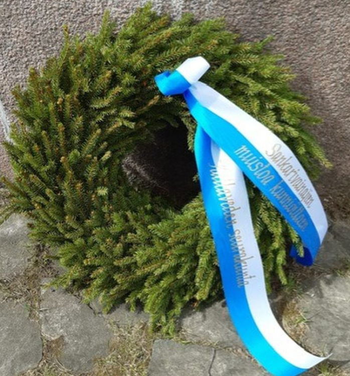 Vihreä havuseppele sinivalkoisella nauhalla. 