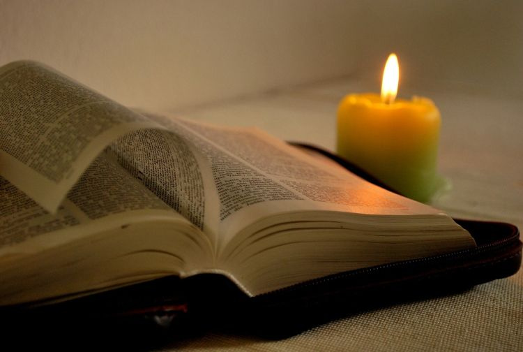 Raamattu, jonka vieressä kynttilä.