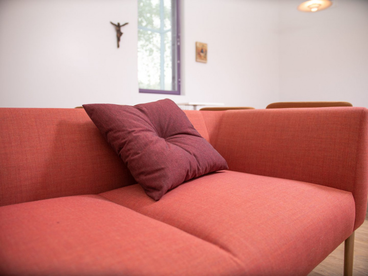 Punainen sohva, jolla punainen tyyny. Seinällä taustalla krusifiksi.