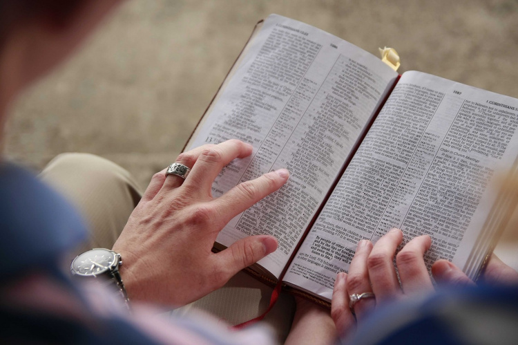 Kuvassa avonainen Raamattu, jonka päällä kaksi kättä.