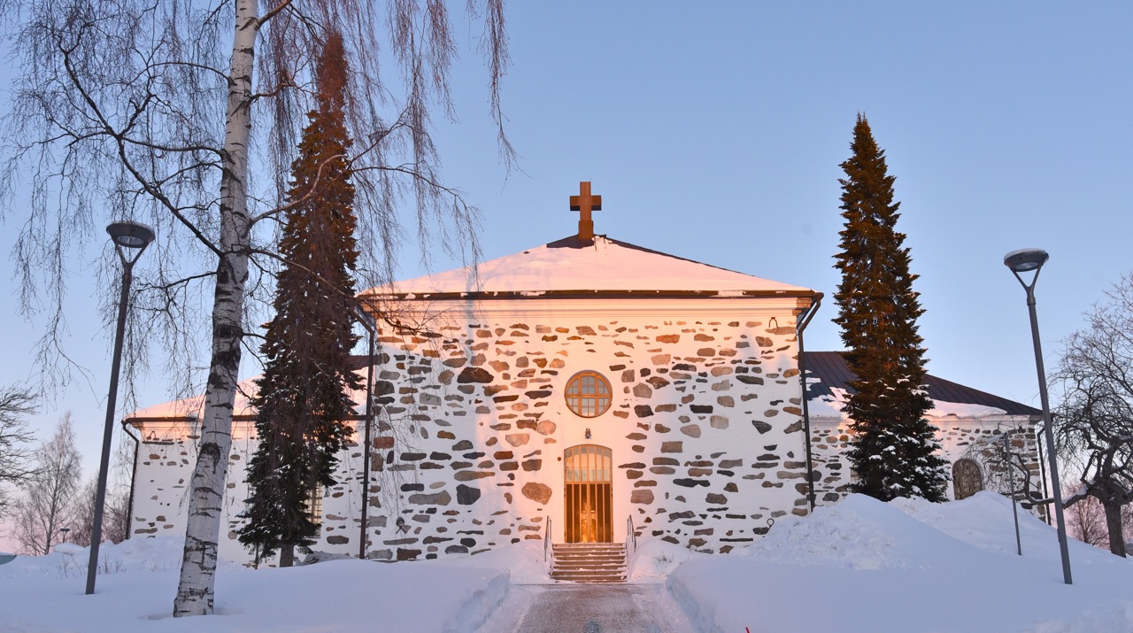 Talvinen maisema, jossa kirkko ja aurinko paistaa.