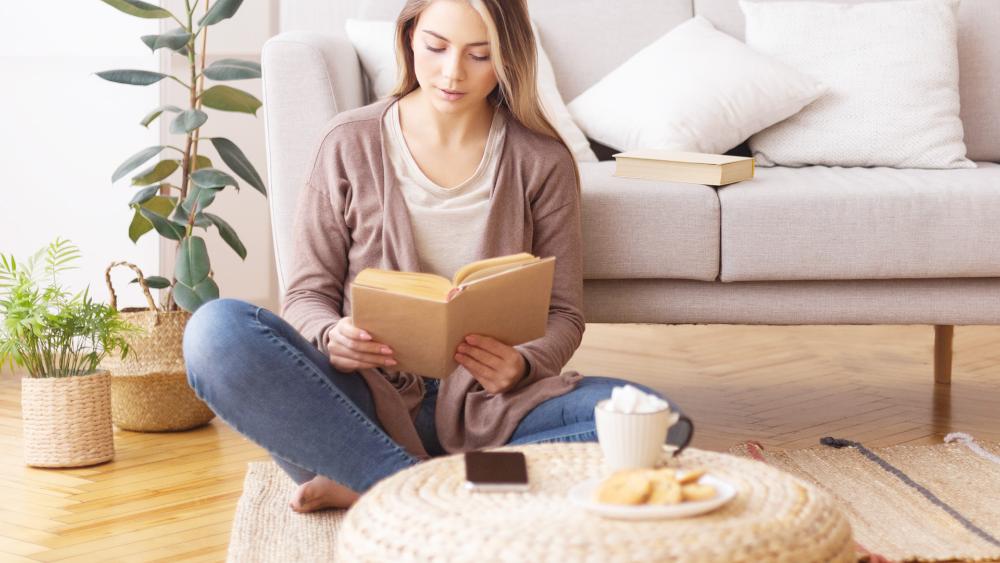 Nuori nainen lukee Raamattua olohuoneessa, edessä puhelin ja kahvikuppi.