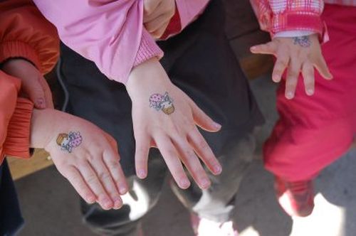 Kolme lasta näyttää oikeaa kättään. Käsissä on värikkäät siirtokuvat.