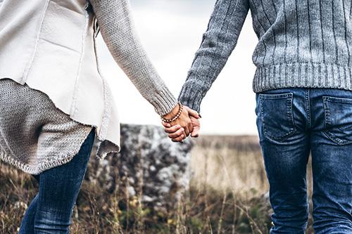 Mies ja nainen kävelevät käsi kädessä pellolla, kuvassa näkyvät yhdessä olevat kädet.