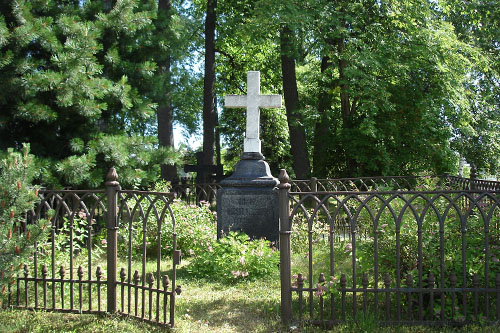 Rauta-aidan takana oleva vanha kivinen muistomerkki, jonka päällä on valkoinen risti.