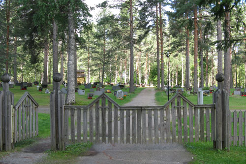 Hautausmaan puinen portti ja näkymä kesäiselle hautausmaalle.