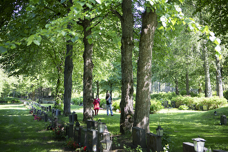 Hautausmaa kesällä, kaksi ihmistä kävelemässä.