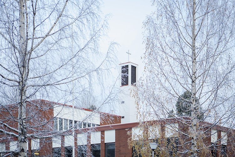 Puijon kirkon torni ja muuta kirkkorakennusta näkyy puiden lehdettömien oksien takaa.