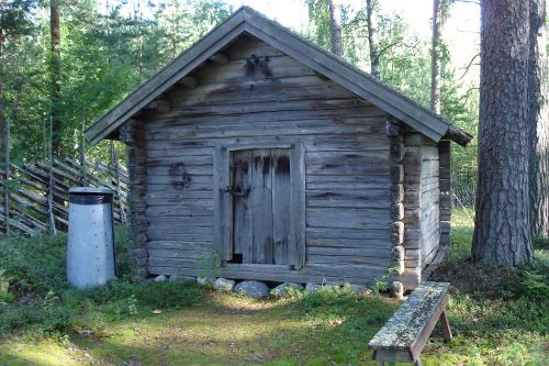 Pieni harmaa hirsinen varastorakennus hautausmaan pisteaidan vieressä. 