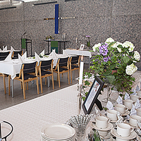 Näkymä Alavan seurakuntasalista: kivinen seinä, pitkä pöytä tuoleineen ja tarjoilupöytä, jonka päällä kahviastiasto ja kukkakimppu.