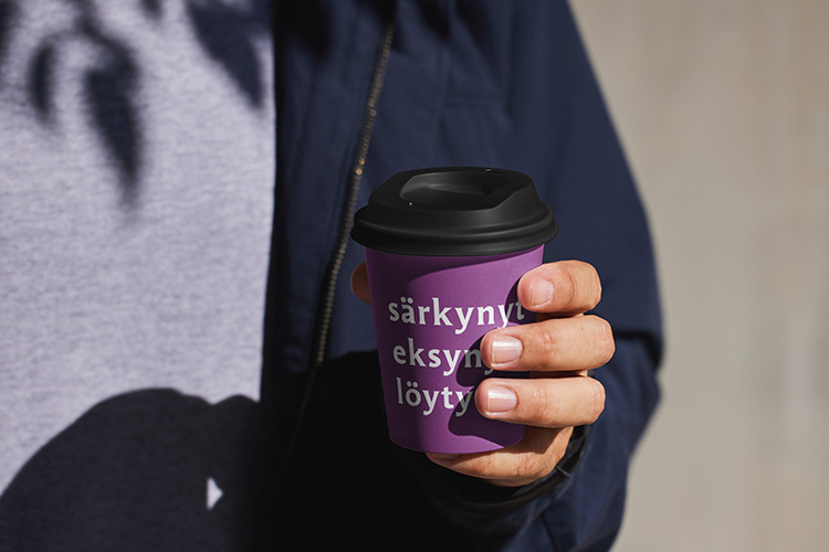 Henkilö kahvikuppi kädessä. Kupissa teksti särkynyt, eksynyt, löytynyt